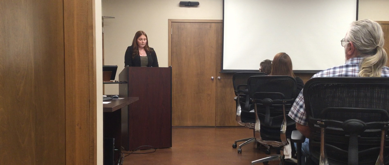 Emma Tuberville, a Youth Leadership Council delegate, presenting at the Ouachita Electric Cooperative board meeting, standing behind a podium in a professional setting with attendees seated and listening attentively.